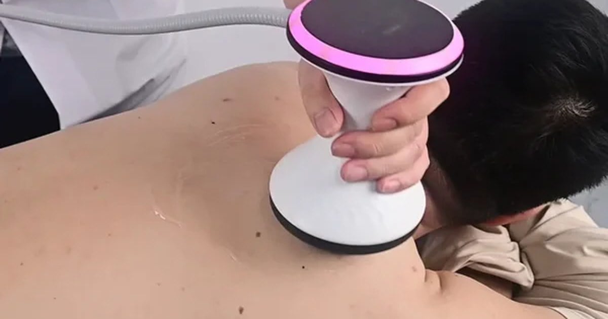 Therapist applying a radial shockwave therapy machine handpiece to a patient's back during a clinical treatment session