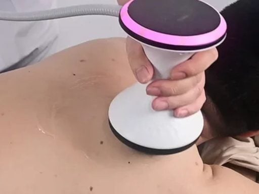 Therapist applying a radial shockwave therapy machine handpiece to a patient's back during a clinical treatment session